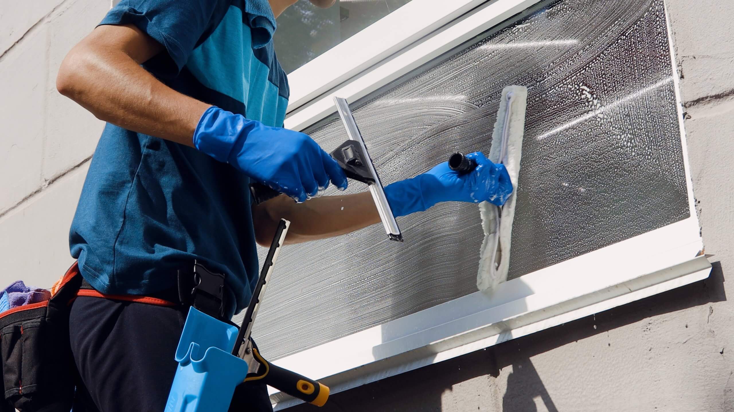 Male professional cleaning service worker in overalls cleans the windows and shop windows of a store with special equipment