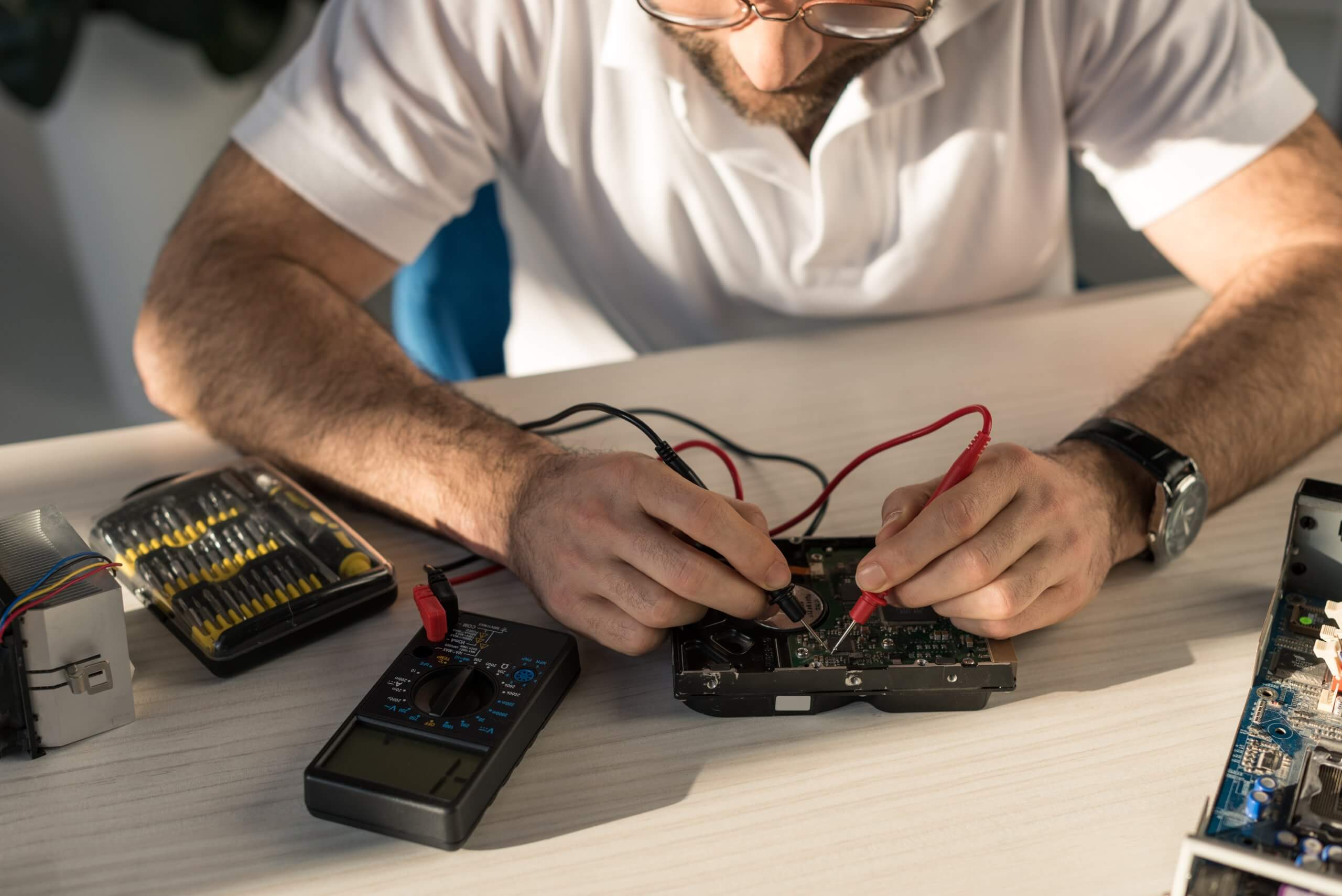man with multimeter checking computer part on table