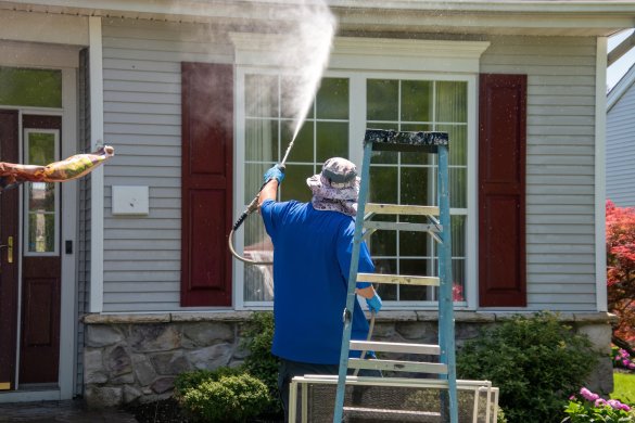 A man using a power washer to clean the windows and front of a house