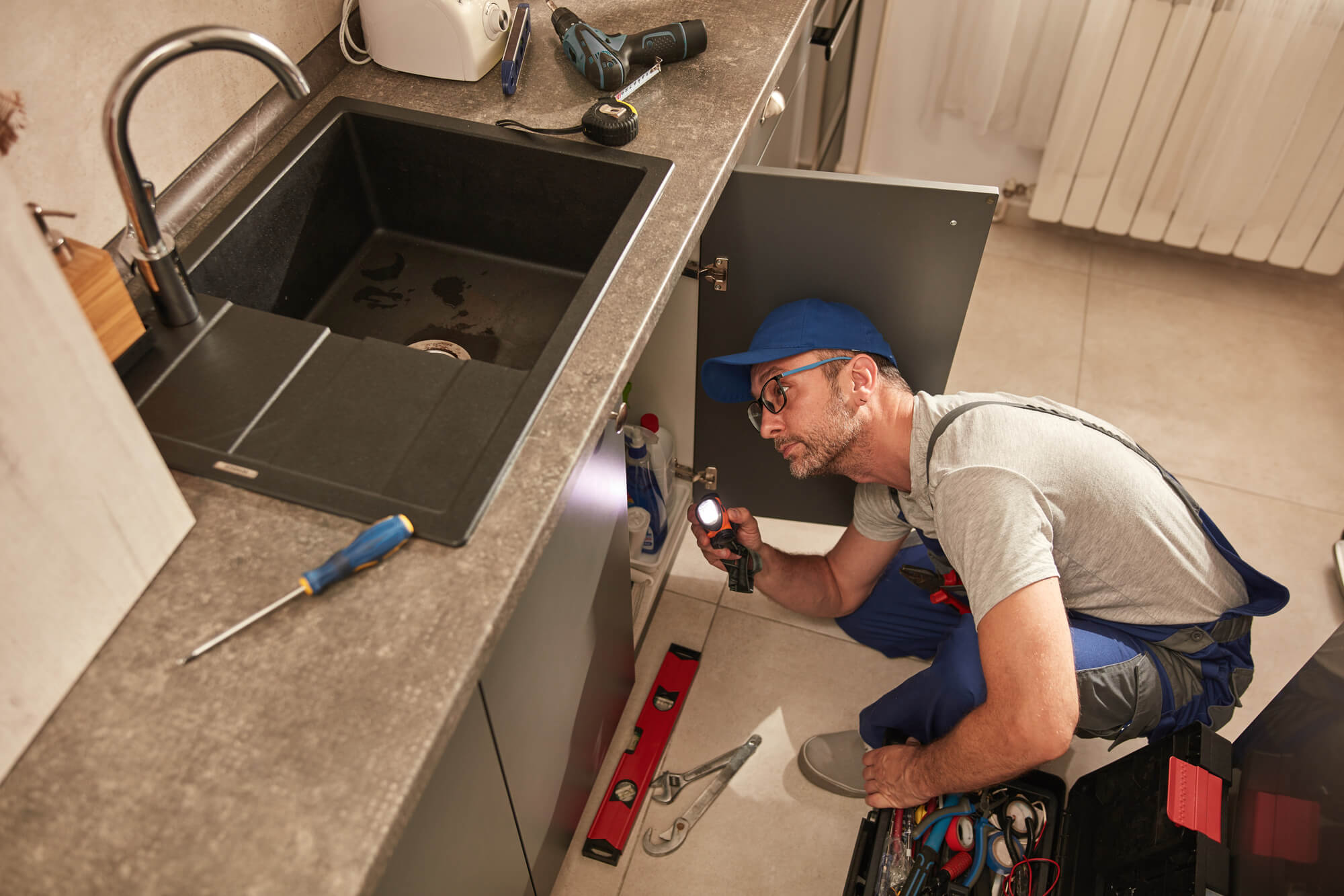 Plumber fixing and repairing water pipes under the kitchen sink.