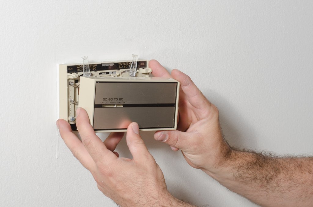 Hands removing and older style thermostat cover.